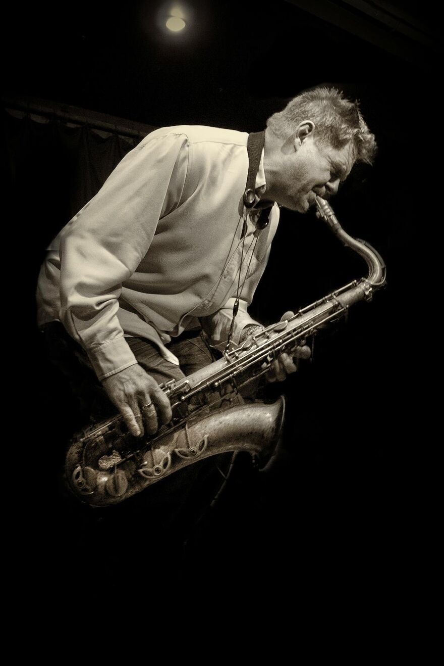 White man, bent over wearing shirt playing saxophone