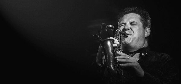 White man blowing sax, black background