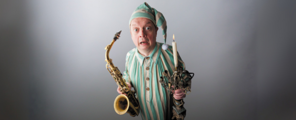 Alan Barnes poses as scrooge with a saxophone in one hand and a candle in the other
