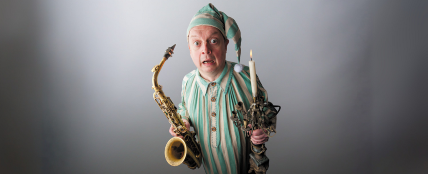 Alan Barnes poses as scrooge with a saxophone in one hand and a candle in the other